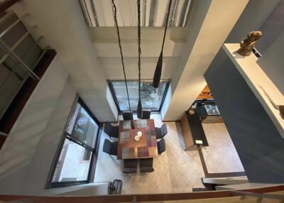 View of a modern dining area from above with a square wooden table, six chairs, large windows, and contemporary lighting