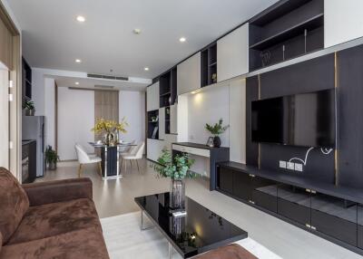 Modern living room with brown sofa, black coffee table, wall-mounted TV, and dining area