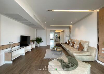 Modern living room with wooden flooring, white shelves, and a comfortable beige sofa.