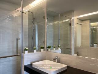 Modern bathroom with a sink, large mirror, glass shower enclosure, and decorative plants.