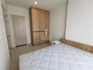 Bedroom with a wooden wardrobe and a bed with a white mattress.