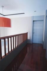 Hallway with wooden flooring and railing, light fixture and door