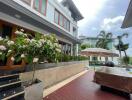 Outdoor patio area of a modern building with covered furniture, a large plant, and an umbrella