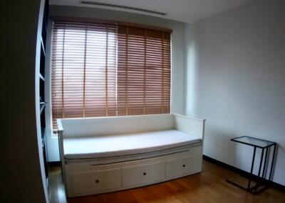 A simple bedroom with a single daybed, wooden floors, window with blinds, and a small side table