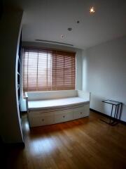 A simple bedroom with a single daybed, wooden floors, window with blinds, and a small side table