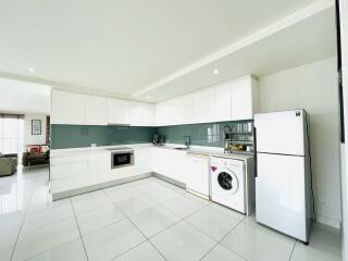 Modern kitchen with white cabinets, appliances including a refrigerator, washing machine, microwave, and dishwasher