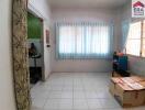 Empty room with tiled floor and windows with blue curtains, adjacent to a workspace