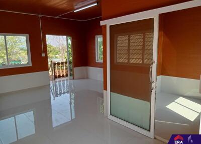 Spacious living area with large windows and sliding glass door, featuring glossy white tile flooring and warm-toned walls