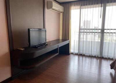 Living room with a wall-mounted TV, wooden flooring, and large windows with curtains