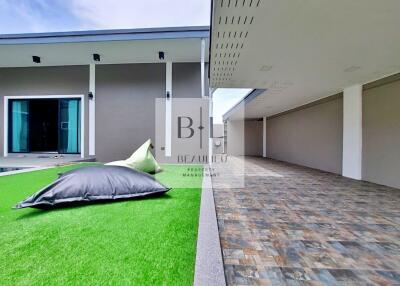 Outdoor area with artificial grass and cushioned seating, adjacent to a building with covered garage space