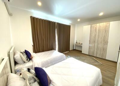 Spacious bedroom with two single beds, large wardrobe, and window covered with brown curtains