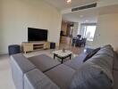 Modern living room with grey L-shaped sofa, flat-screen TV, and view into dining area and kitchen