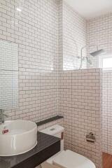 Modern white-tiled bathroom with a vessel sink and glass shower
