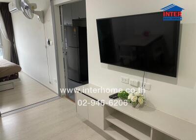 Main living space with wall-mounted TV and view into kitchen and bedroom