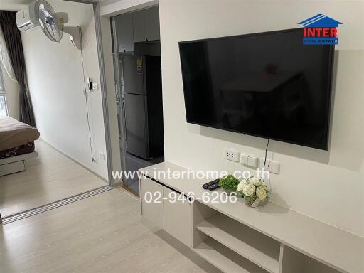 Main living space with wall-mounted TV and view into kitchen and bedroom