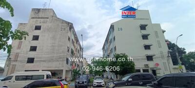 Two multi-story residential buildings with parked vehicles in front