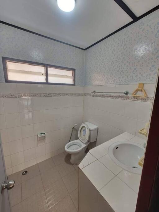 Bathroom with tiled walls, a toilet, sink, and frosted windows