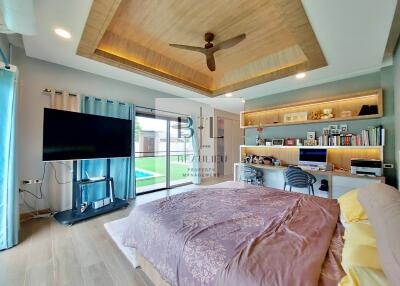 Spacious bedroom with modern decor, built-in shelves, a desk, TV, and large windows overlooking a garden