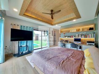 Spacious bedroom with modern decor, built-in shelves, a desk, TV, and large windows overlooking a garden