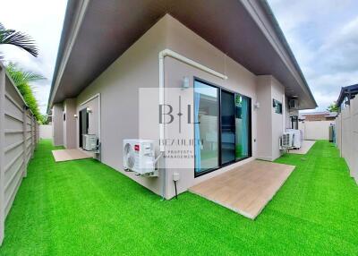 photo of the exterior of a residential building with green artificial grass, air conditioning units, and sliding glass doors