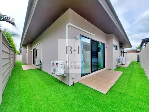 photo of the exterior of a residential building with green artificial grass, air conditioning units, and sliding glass doors