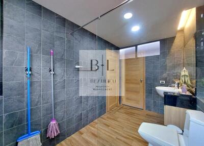 Modern bathroom with wooden flooring, black tiled walls, a shower, toilet, and sink.