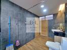 Modern bathroom with wooden flooring, black tiled walls, a shower, toilet, and sink.