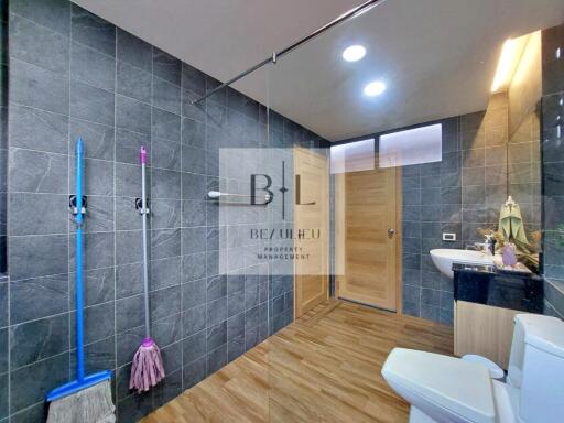 Modern bathroom with wooden flooring, black tiled walls, a shower, toilet, and sink.