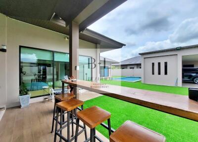 Modern outdoor space with wooden bar stools, green lawn, and pool