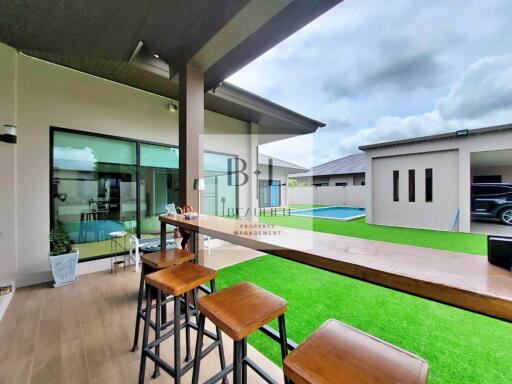 Modern outdoor space with wooden bar stools, green lawn, and pool