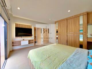 Spacious bedroom with large bed, wall-mounted TV, built-in wooden wardrobes, and sliding glass doors.