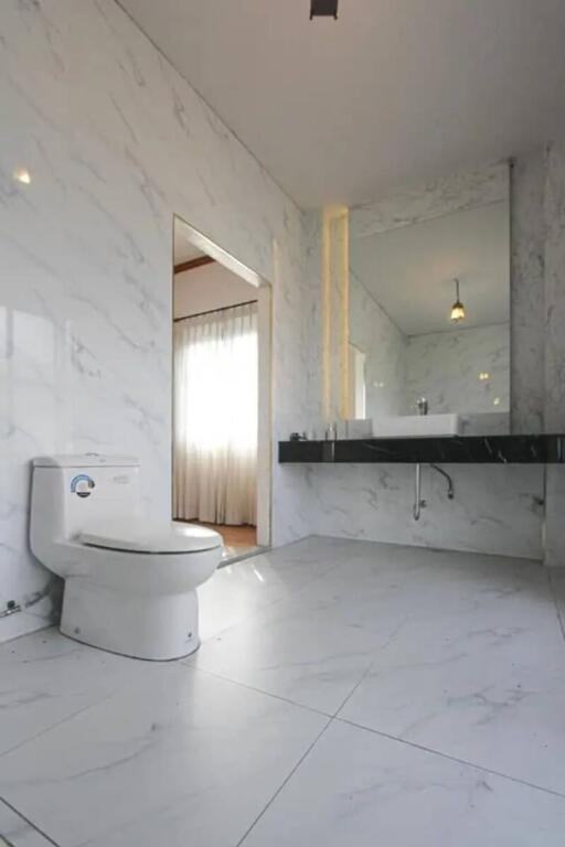 Modern bathroom with marble tiles, a toilet, and a sink with a mirror