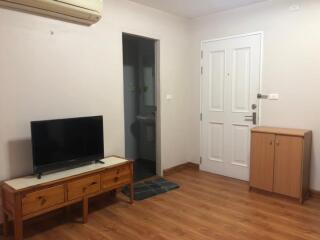 Living room with TV, wooden furniture, and door leading to bathroom