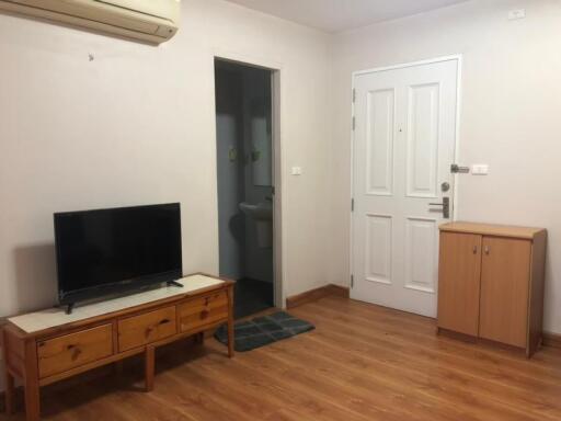 Living room with TV, wooden furniture, and door leading to bathroom