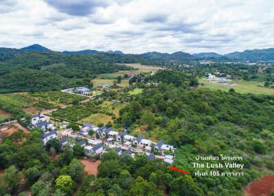 Aerial view of a housing development in a lush valley area with surrounding mountains and greenery