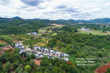 Aerial view of a housing development in a lush valley area with surrounding mountains and greenery