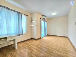 A spacious bedroom with wooden floor, windows with curtains, and an air conditioner.