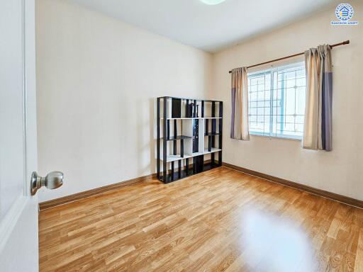 Empty bedroom with wooden flooring, a bookshelf, and windows with curtains