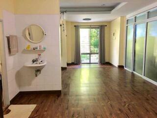 Well-lit main living space with wooden flooring and adjoining bathroom.