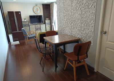 Dining area with a wooden floor, table, and chairs, adjacent to a living space with a TV