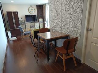 Dining area with a wooden floor, table, and chairs, adjacent to a living space with a TV