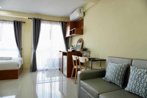 Modern studio apartment with bed, sofa, dining area, and large windows.