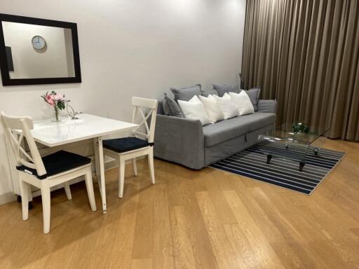 Living room with a gray sofa, glass coffee table, and small dining area