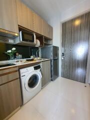 Compact kitchen with wooden cabinets, washing machine, microwave, fridge, and sink area