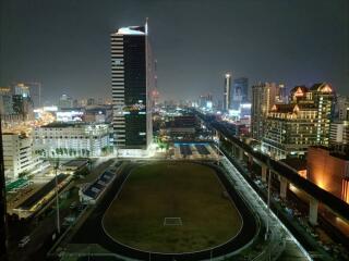 Nighttime view of a cityscape with illuminated buildings and a sports stadium in the foreground.