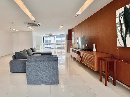 Spacious and modern living room with grey sectional sofa, wall-mounted TV, and contemporary decor.