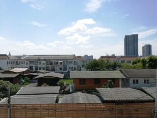 View of residential area with various buildings and a distant high-rise under a clear sky