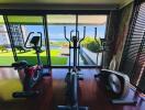 Modern fitness room with exercise equipment and large windows with a garden view