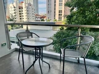 Balcony with table and chairs, overlooking a cityscape with trees and buildings