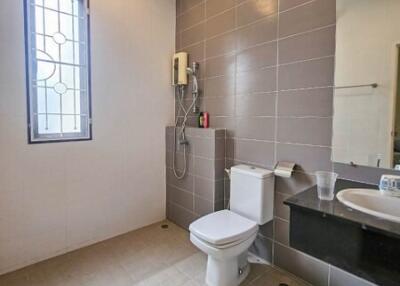 Modern bathroom with tiled walls and floors, featuring a toilet, sink, mirror, and shower